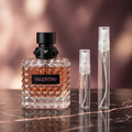 Valentino Donna Born in Roma Intense bottle beside clear glass 5 ml and 10 ml travel sprays in a rose-toned marble setting